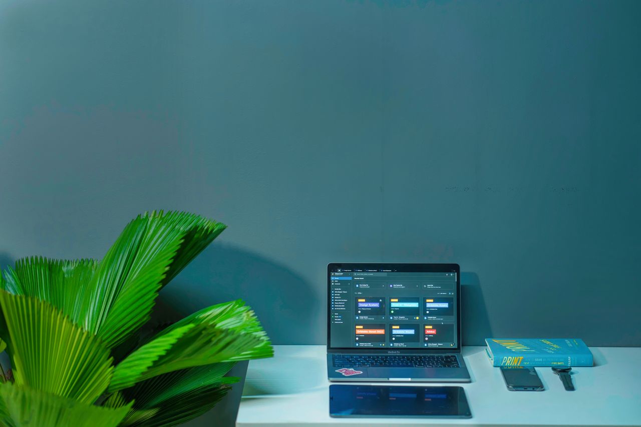 Home Sleek office desk setup featuring a laptop, tropical plant, and book in a modern design.