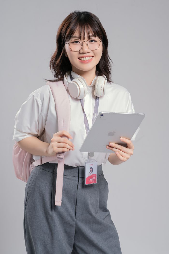 Smiling young woman holding a tablet with headphones around neck and backpack.