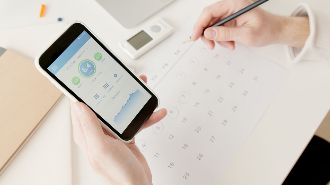 Home Close-up of hands using a smartphone to track health stats while planning on a calendar.