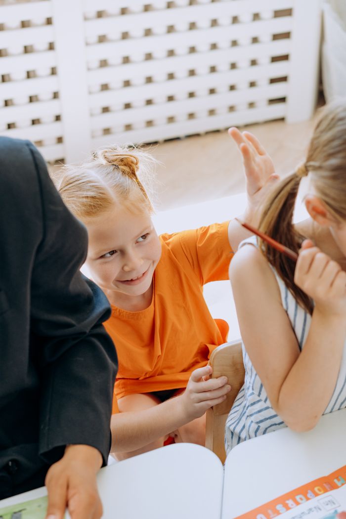 Two young girls having fun while sitting at a classroom table, engaged in playful learning activities.