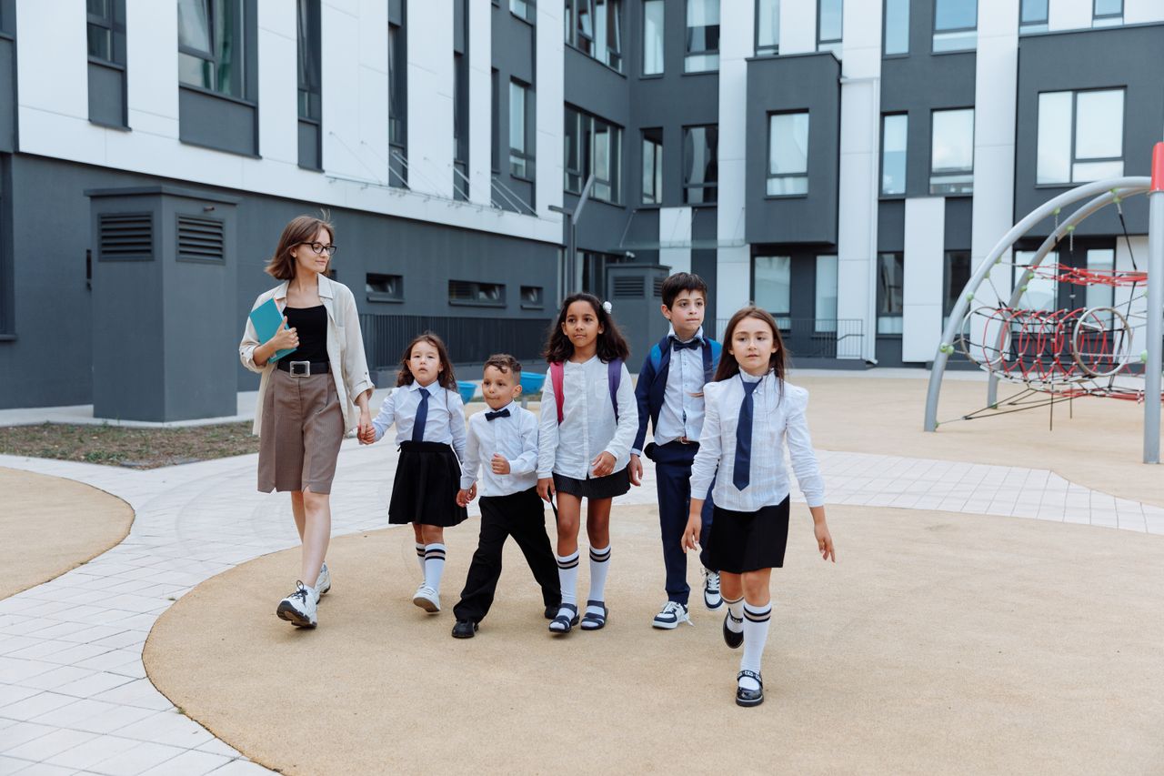 A teacher leading a group of diverse students on a modern school campus walkway.